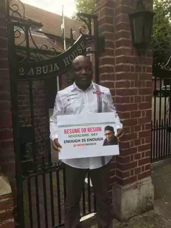 Resume Or Resign: Man Pictured Standing In Front Of Abuja House In London With Placard